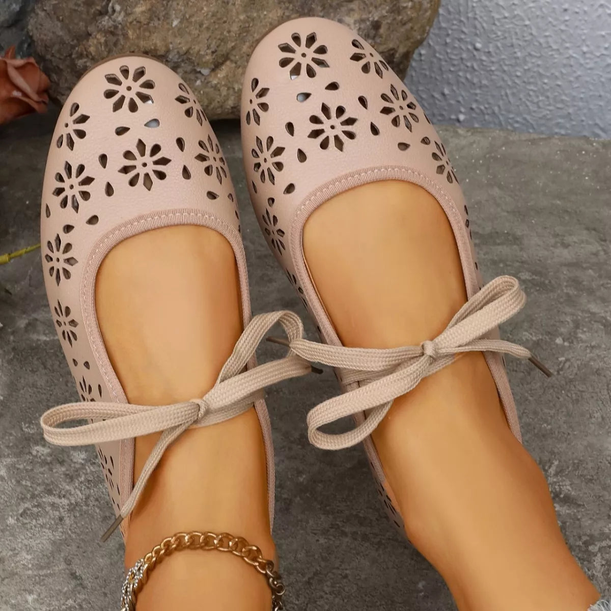 Pair of pink ballet flats with floral cutouts on a stone surface