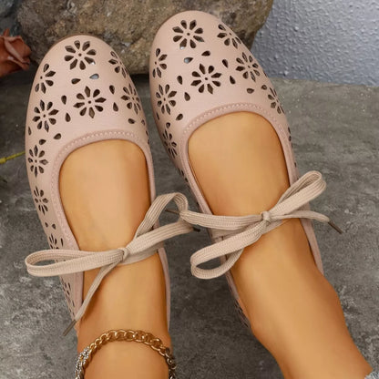 Pair of pink ballet flats with floral cutouts on a stone surface
