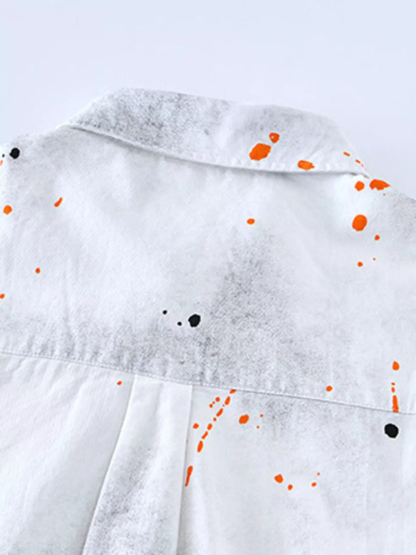 White shirt with orange and black paint splatter design on a light gray background