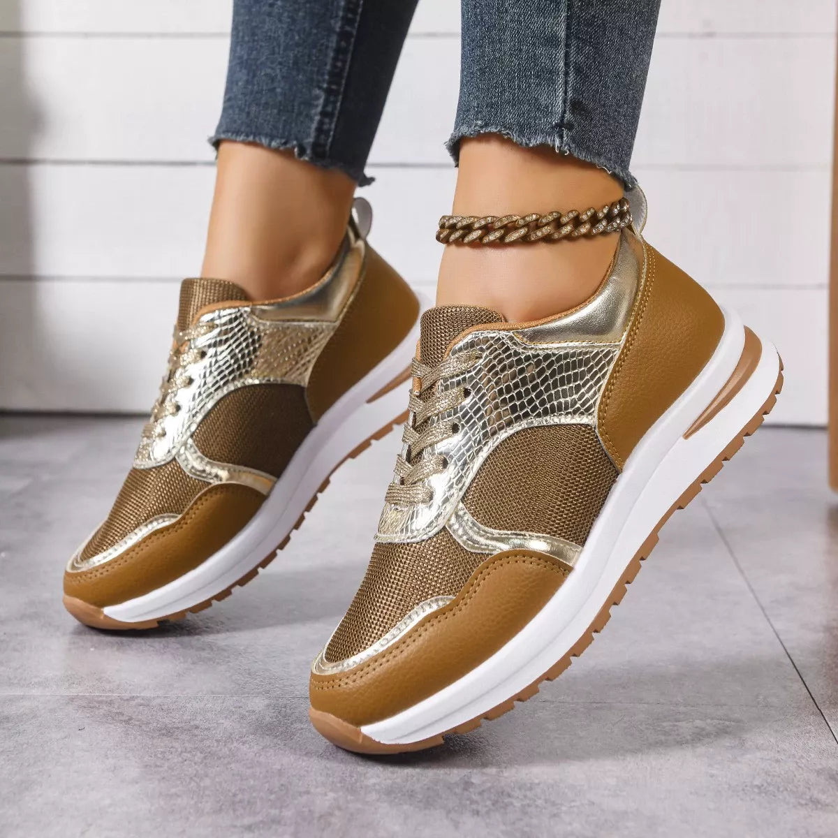 Brown and gold sneakers worn with blue jeans on a light gray floor.