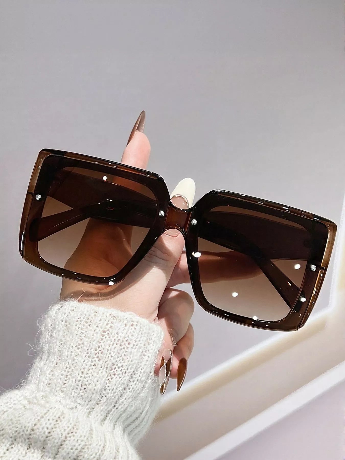 Sunglasses held by a hand with a neutral background