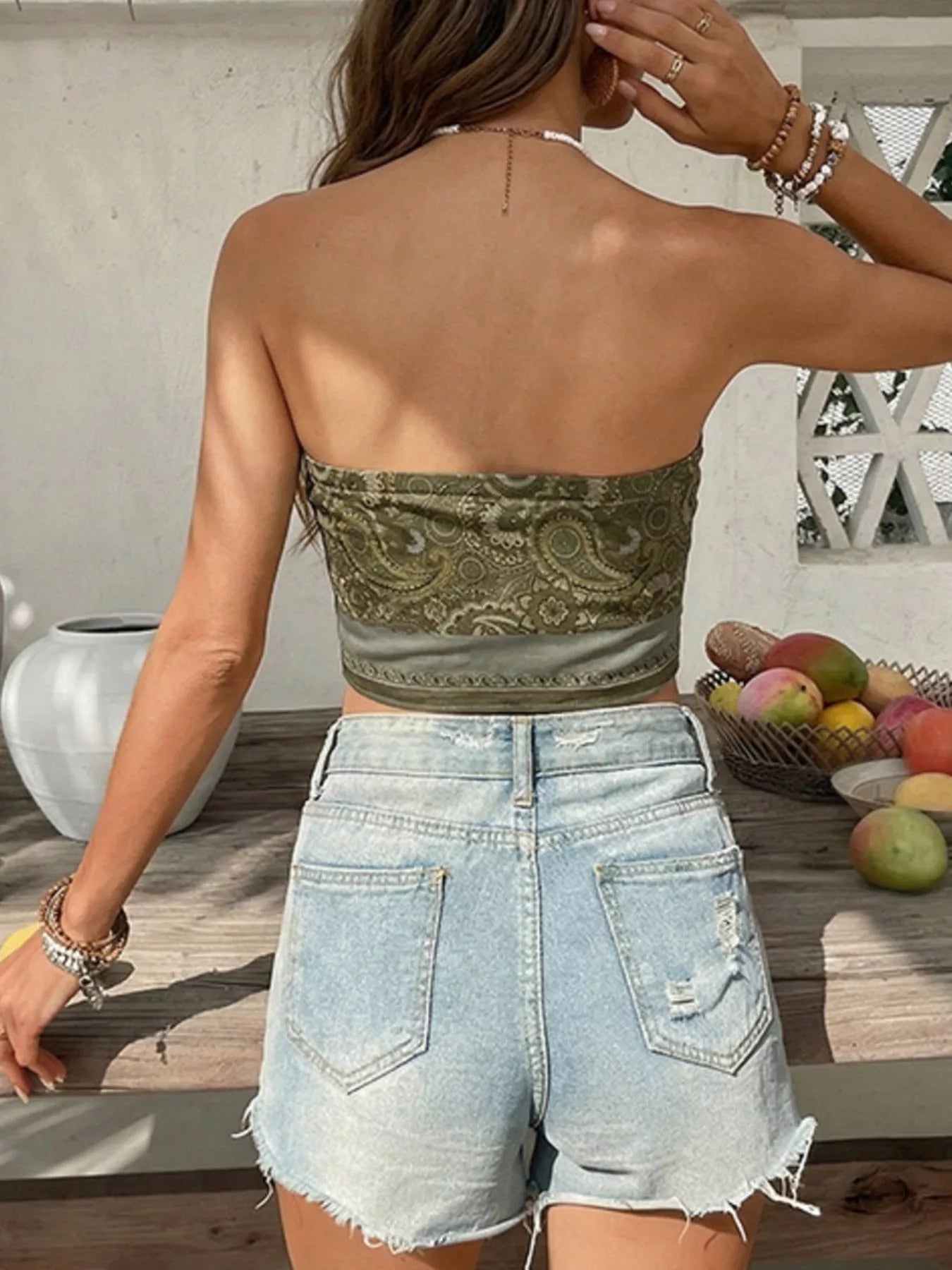 Person wearing a green patterned strapless top and denim shorts outdoors.