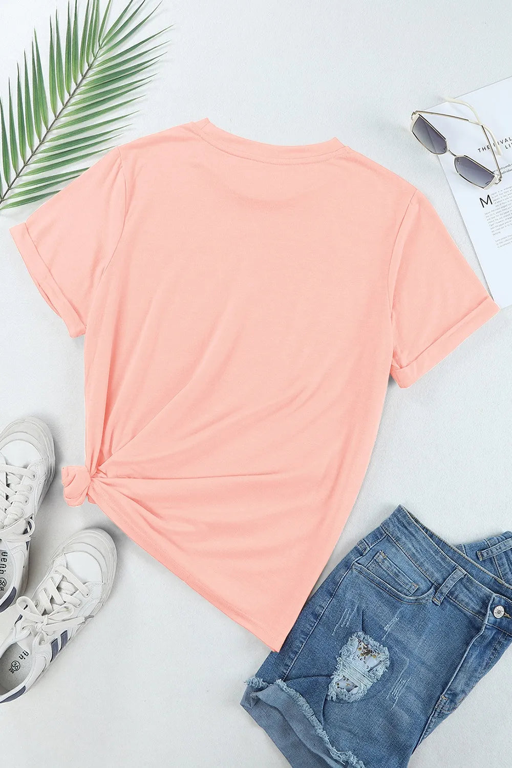 Peach t-shirt with sunglasses, sneakers, and jeans on a light gray background