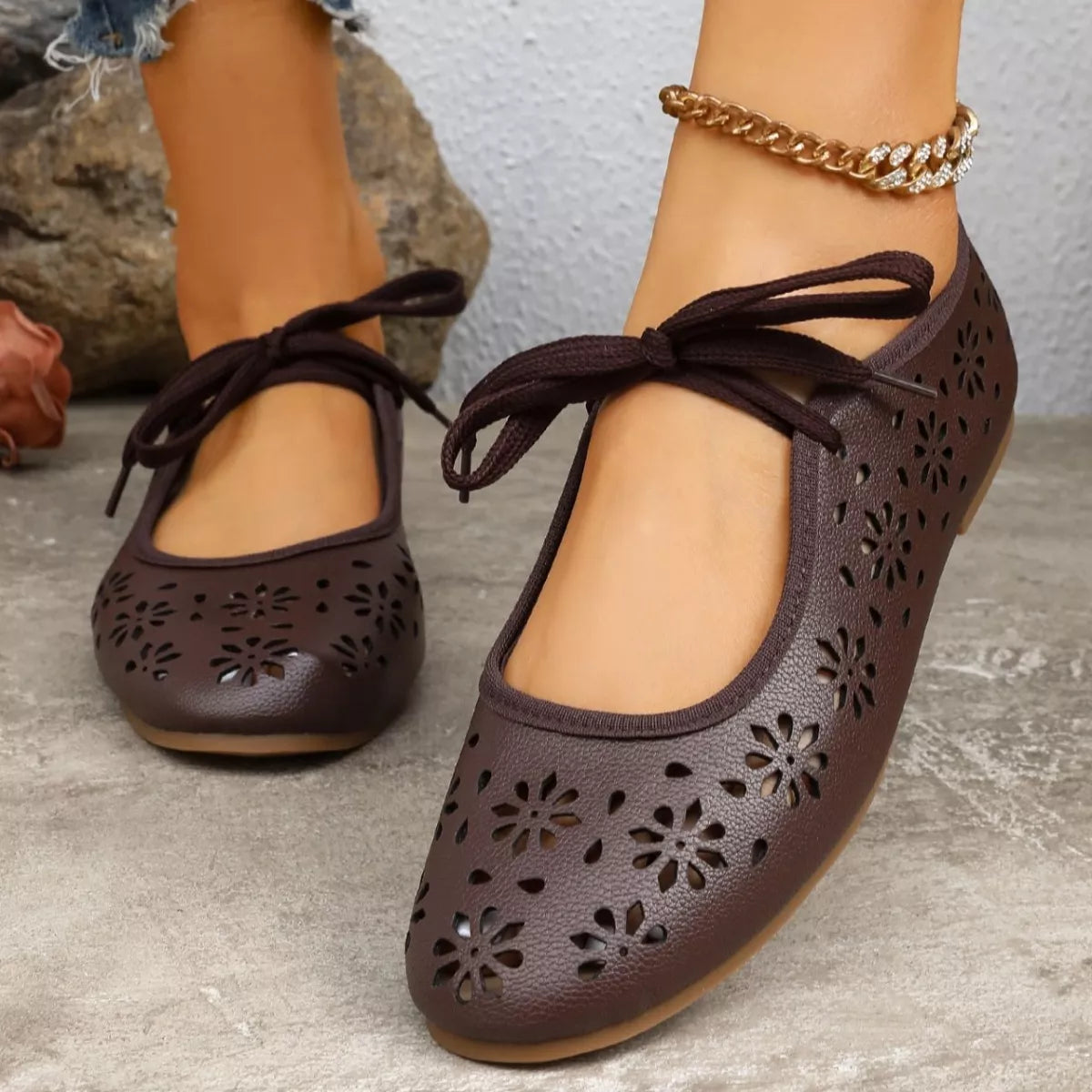 Brown perforated shoes with bow details on a stone surface.