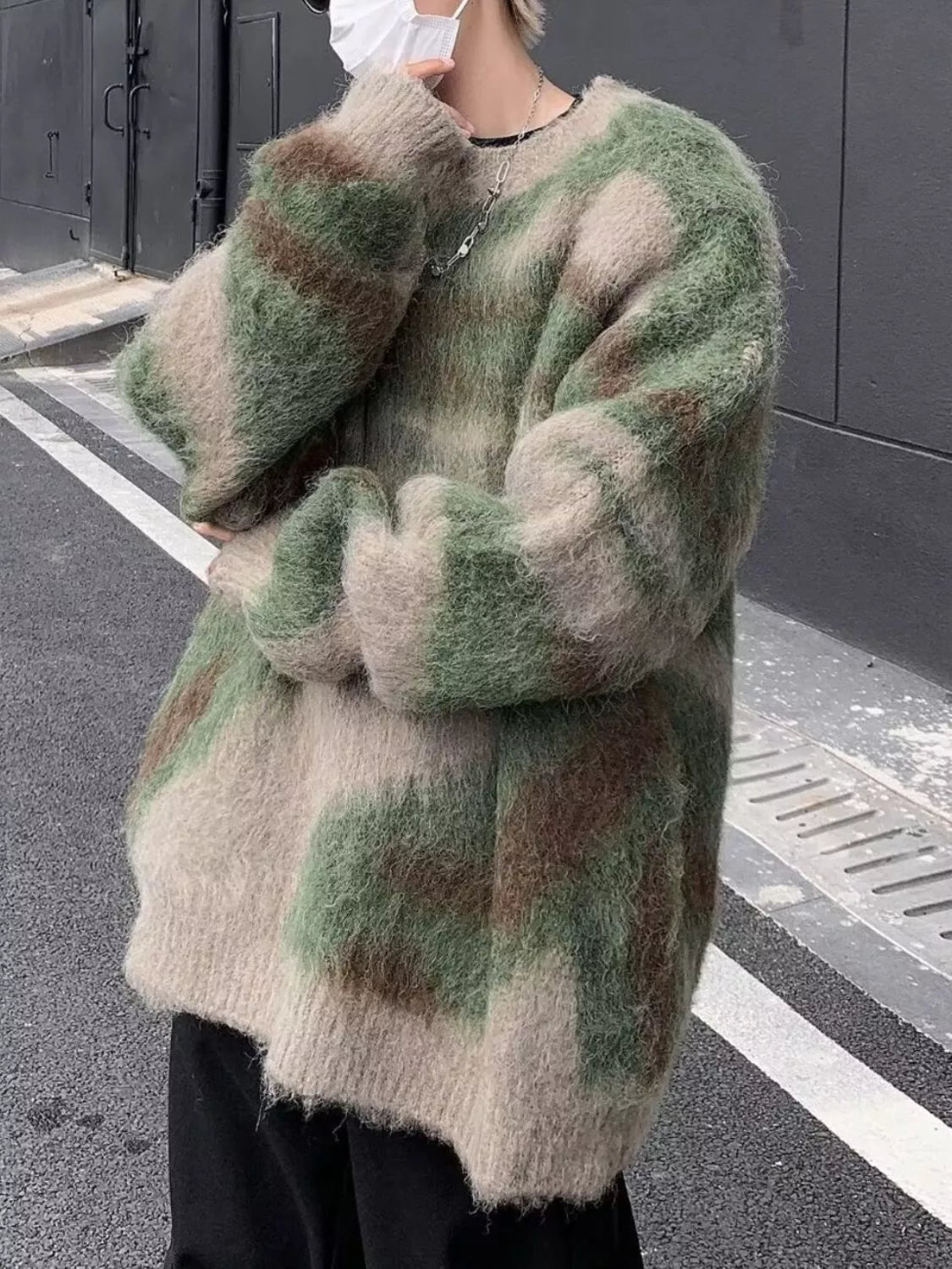 Person wearing a camouflage-patterned sweater on a street.