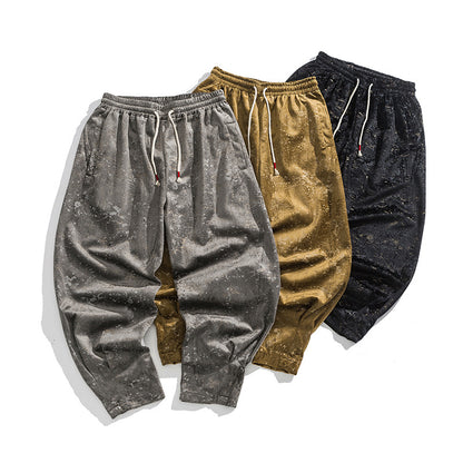 Three pairs of velvet jogger pants in gray, gold, and black on a white background.