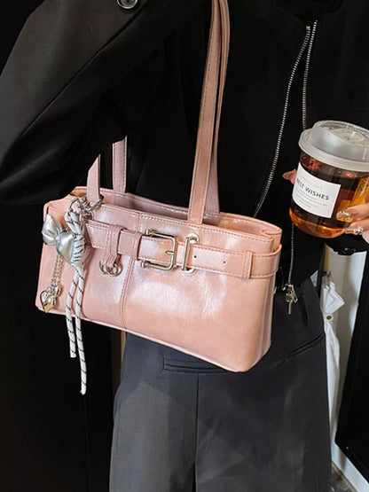 Person holding a pink handbag with decorative elements and a drink.