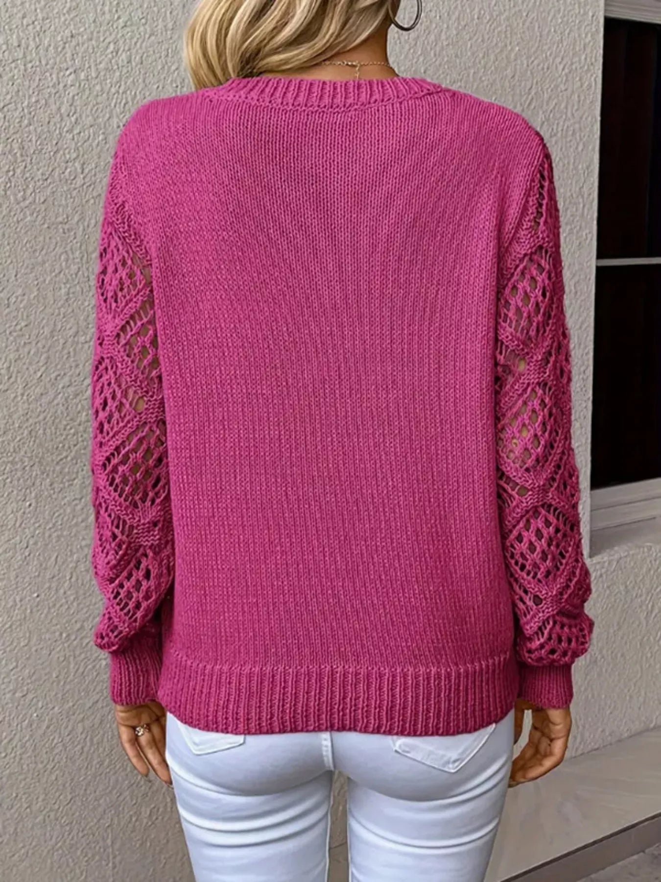 Person wearing a pink sweater with lace sleeves against a neutral wall.