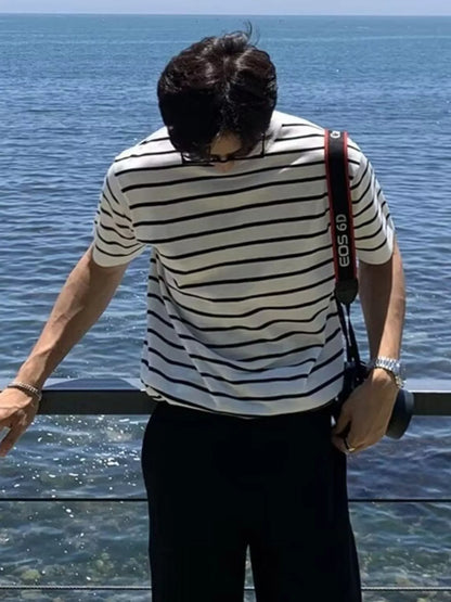 Person wearing a striped shirt with a camera around their neck, standing by a body of water.