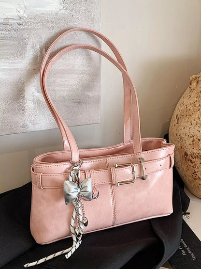 Pink handbag with decorative bow charm on a black surface