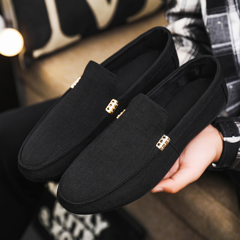 Black loafers with gold accents held by a person in a plaid shirt.