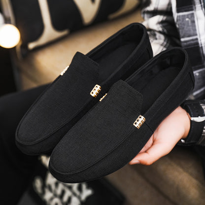 Black loafers with gold accents held by a person in a plaid shirt.
