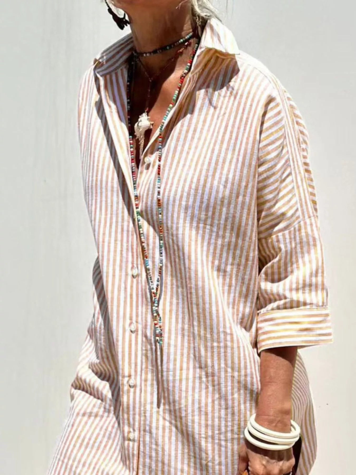Person wearing a striped shirt with rolled-up sleeves against a plain background