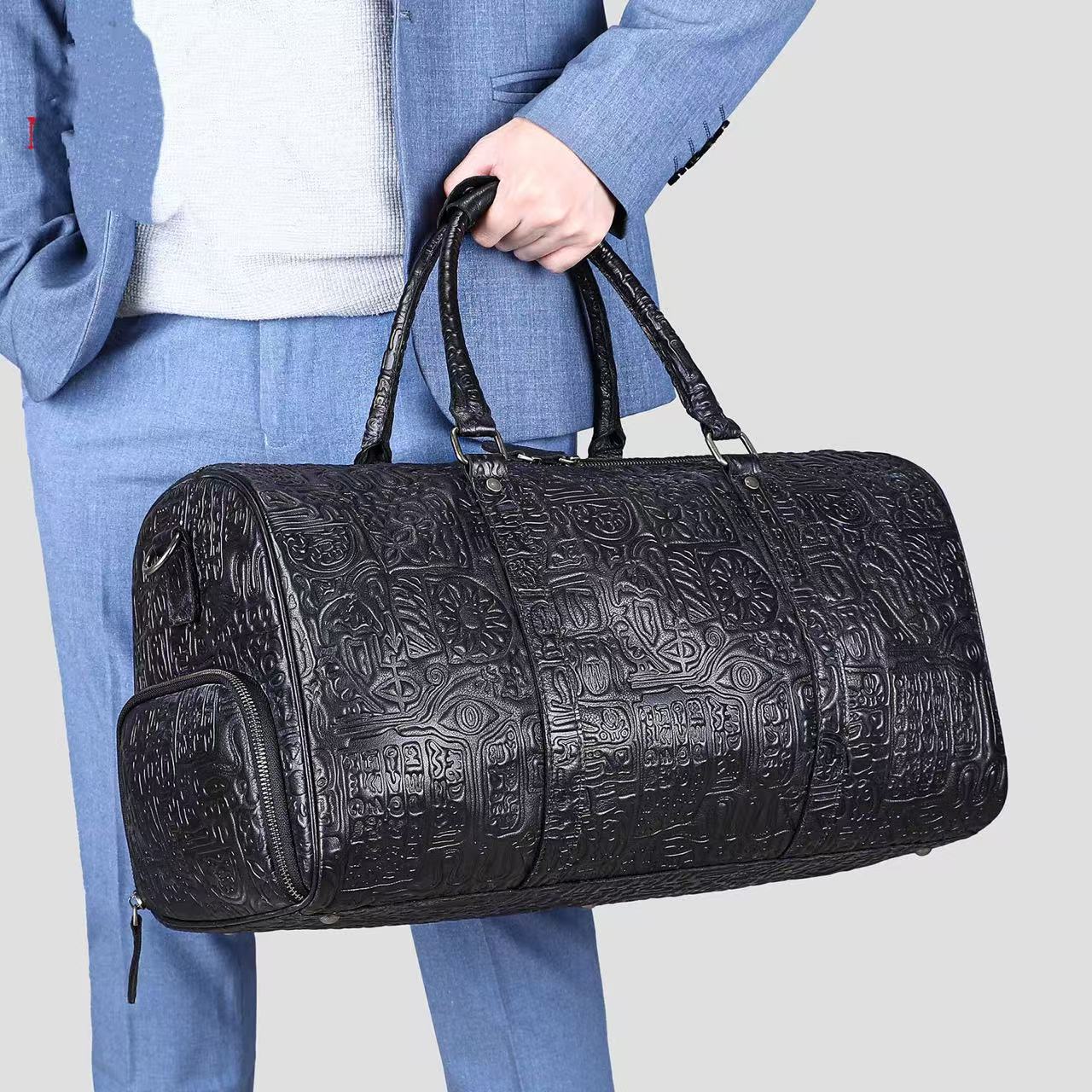 Person holding a black embossed duffel bag against a light gray background