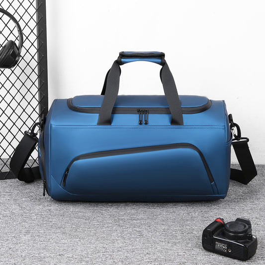 Blue duffel bag with black straps on a gray floor, with headphones and a camera in the background.