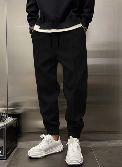 Person wearing black jogger pants and white sneakers against a neutral background