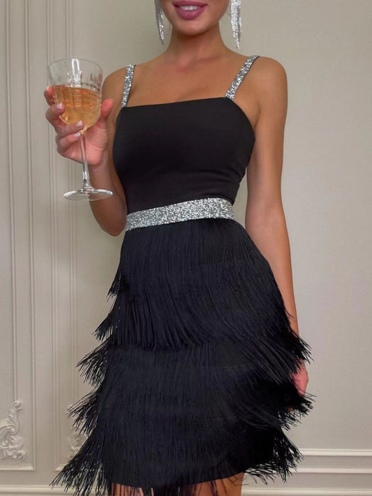 Black dress with fringe skirt and silver waistband held by a person against a neutral background