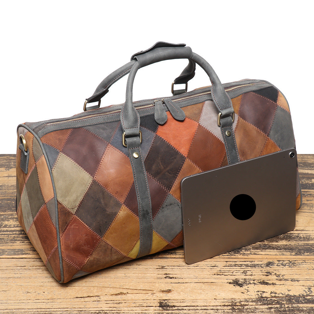 Patchwork leather duffel bag on a wooden surface with a tablet propped against it.