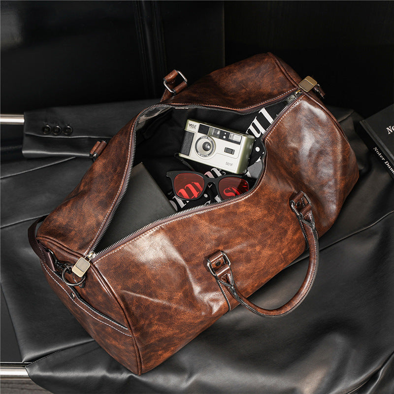 Brown leather duffel bag with vintage camera and items on a black surface