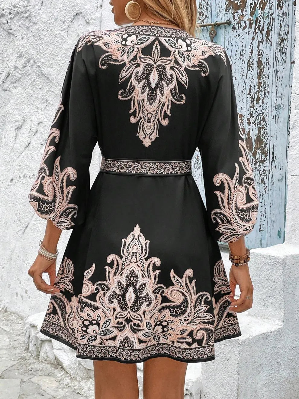 Black dress with intricate white and beige patterns worn by a person against a textured wall.
