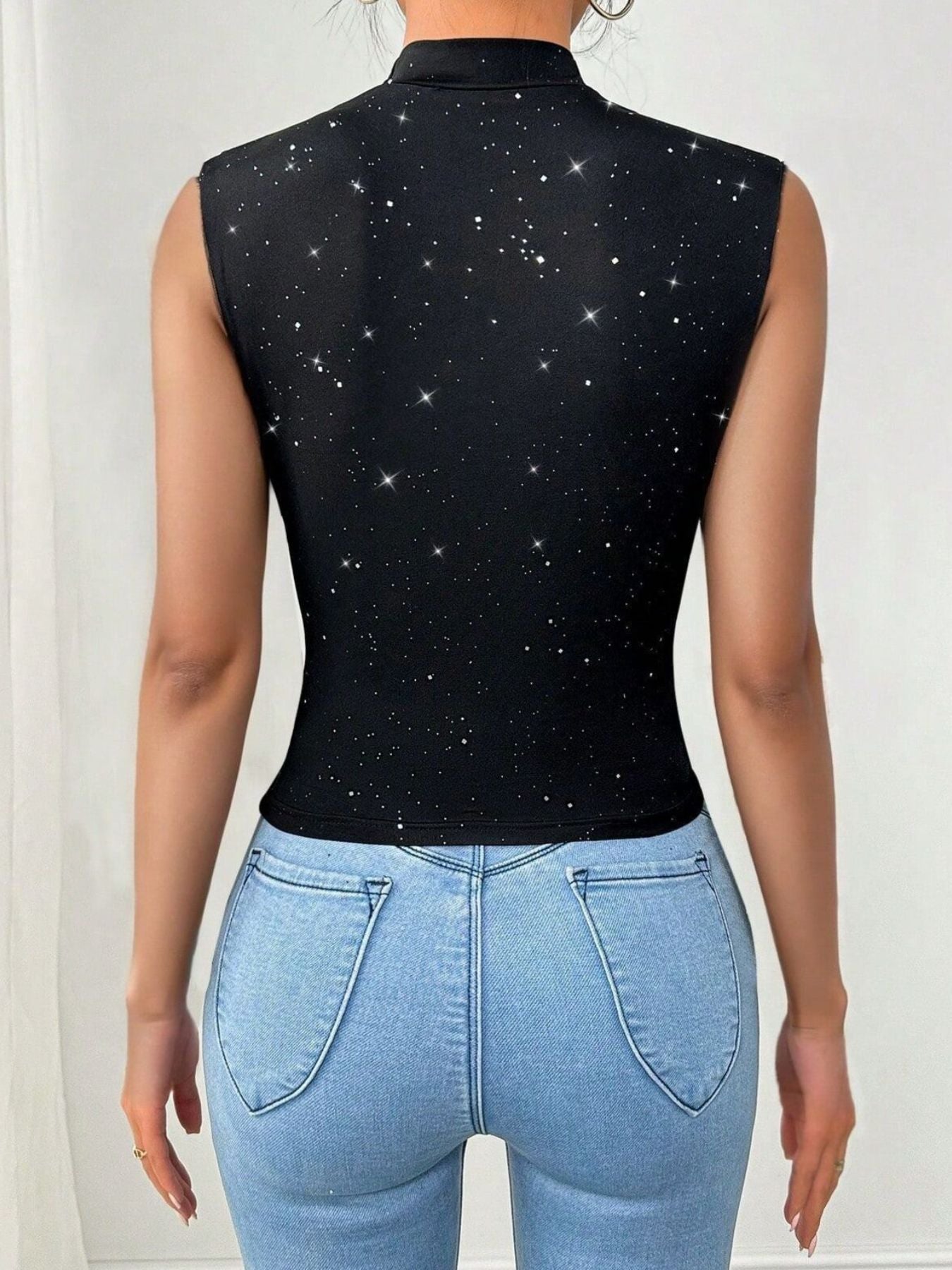 Person wearing a black sleeveless top with star pattern and light blue jeans on a white background