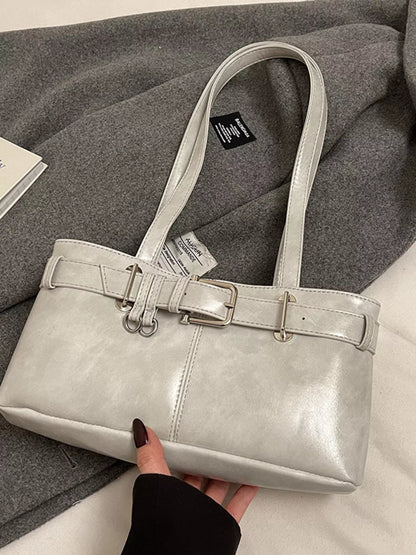 Silver handbag with a belt buckle held by a hand on a gray fabric background