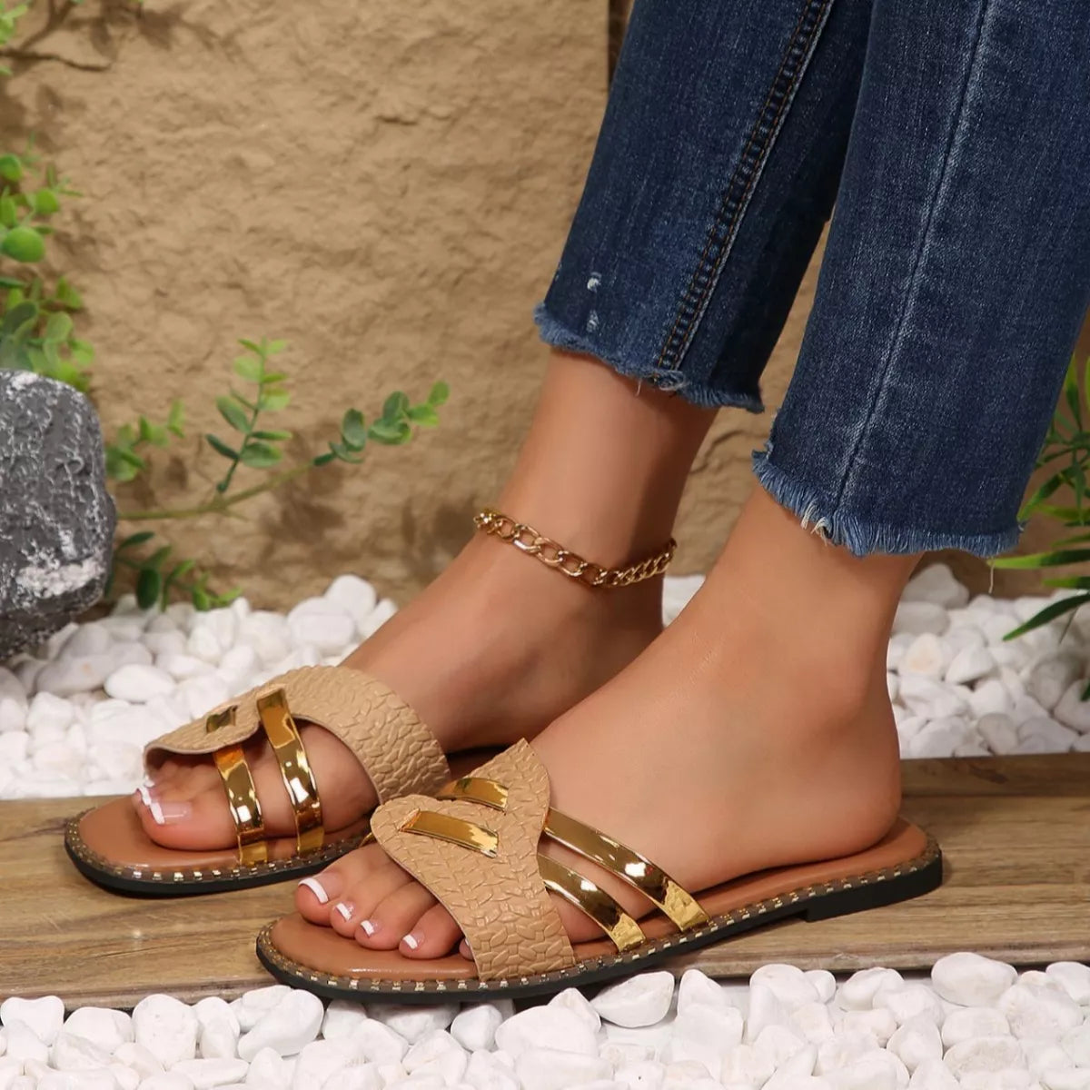 Beige sandals with gold accents worn by a person on a pebbled surface.