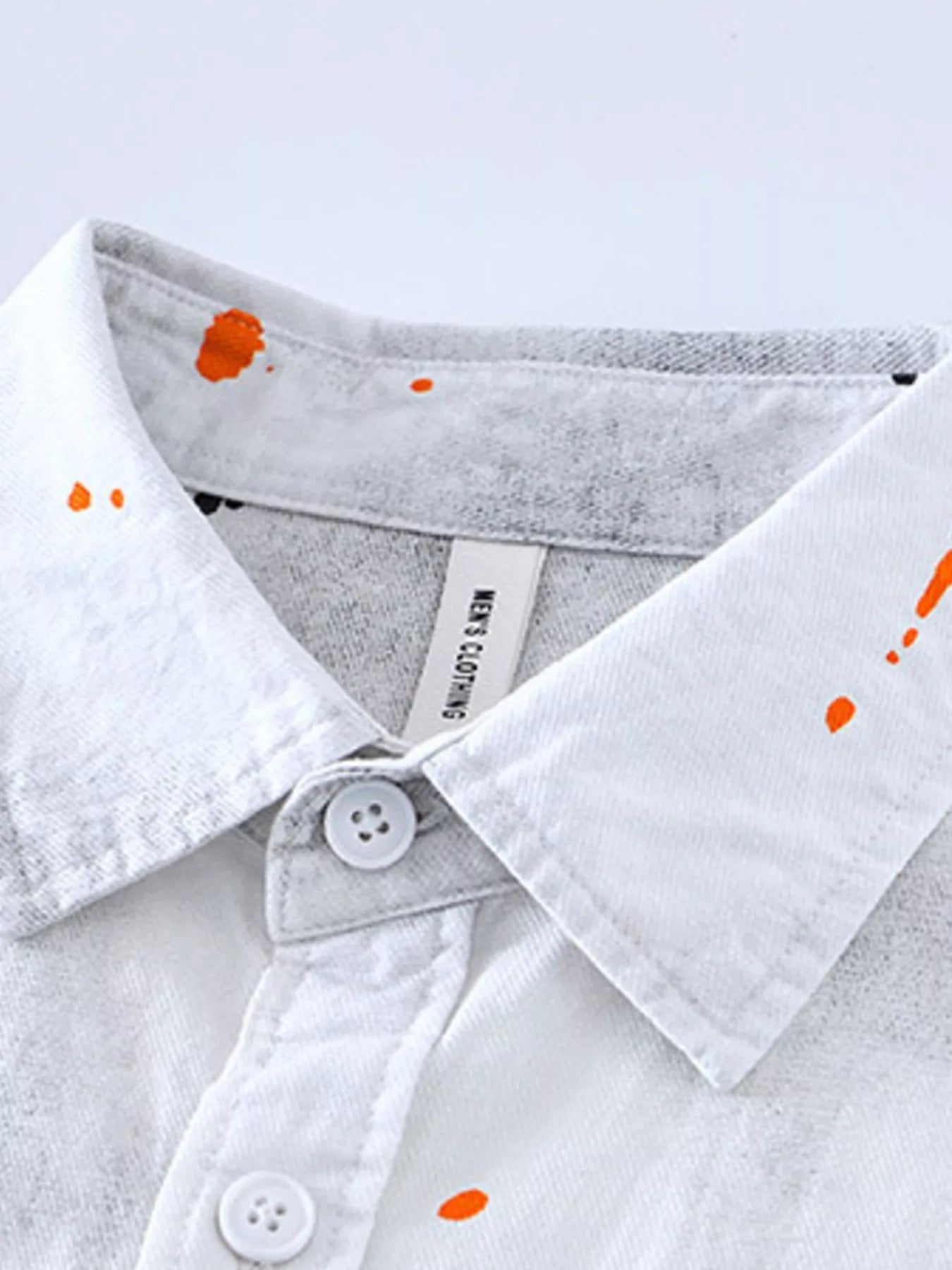 Close-up of a white shirt with orange paint splashes on a light gray background