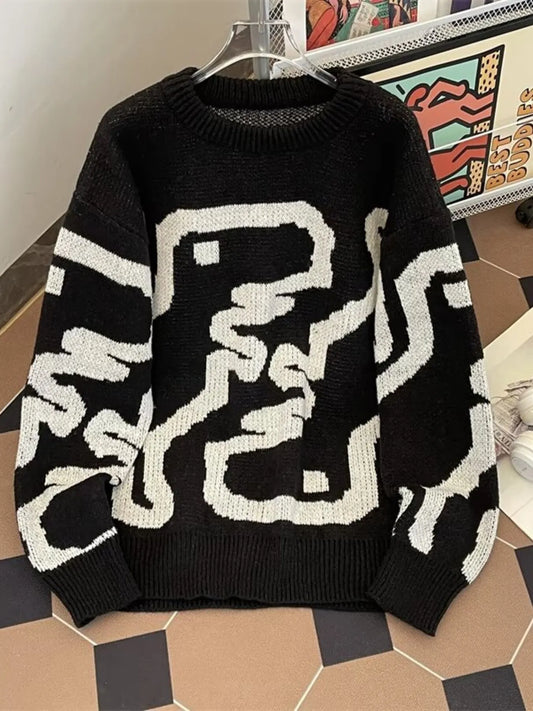 Black sweater with white geometric pattern on a hanger against a colorful abstract painting background.