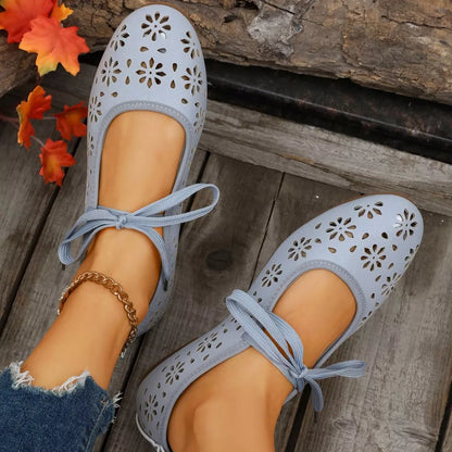 Blue perforated shoes with lace-up design worn by a person on a stone surface.