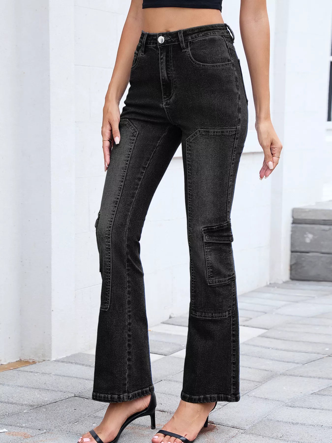 Person wearing black flared jeans standing on a stone floor with a white wall background