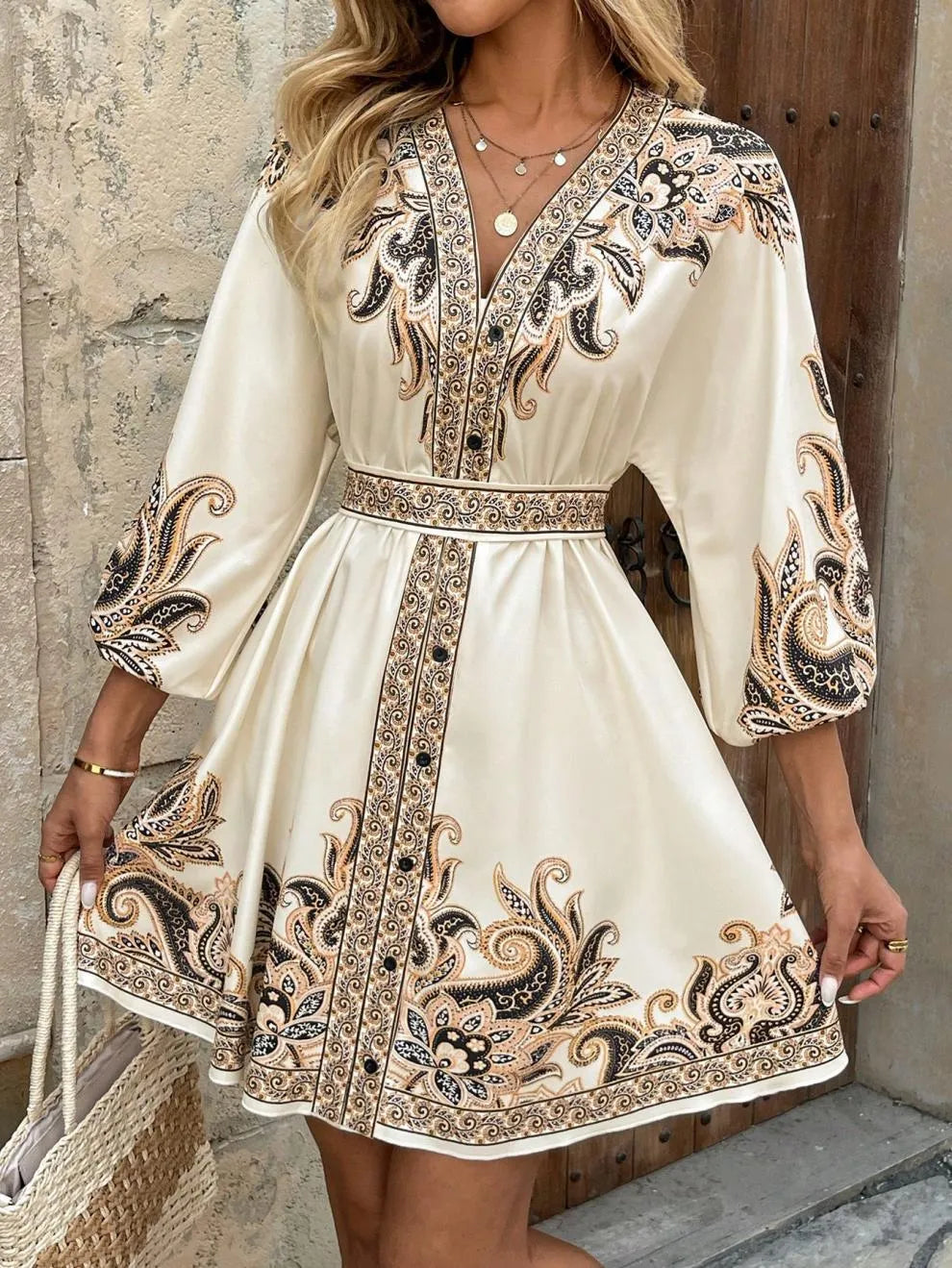 Woman wearing a white dress with black and gold embroidery against a stone wall.