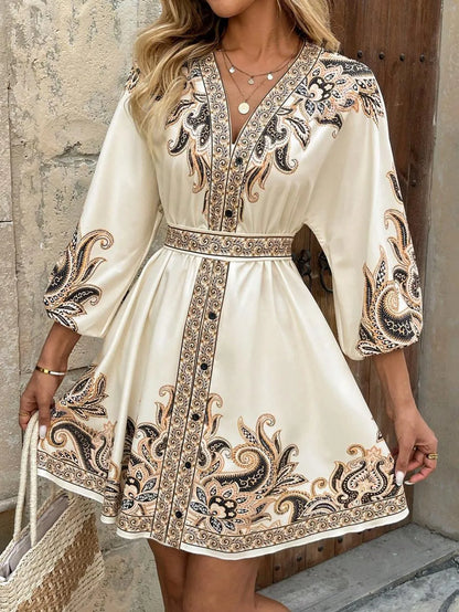 Woman wearing a white dress with black and gold embroidery against a stone wall.