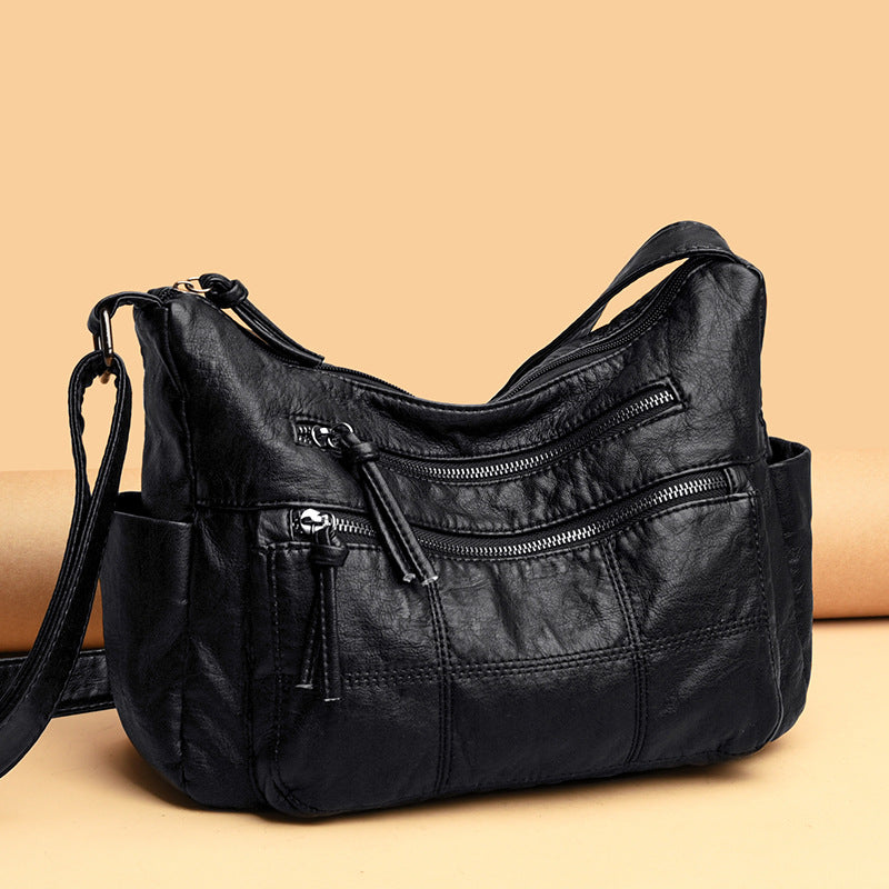 Black leather handbag with multiple zippers on a beige background