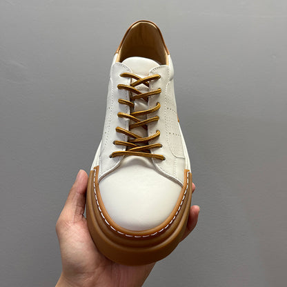 White sneaker with brown accents held by a hand against a gray background