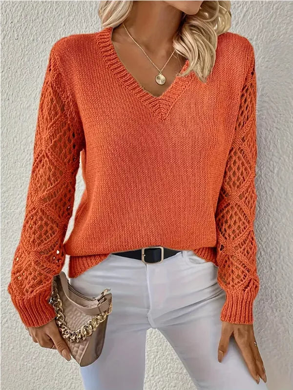 Person wearing an orange knitted sweater with a textured pattern, white pants, and holding a brown handbag against a plain background.
