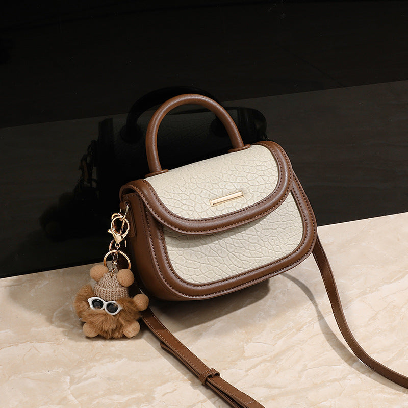 Small handbag with a brown strap and a keychain on a light surface.