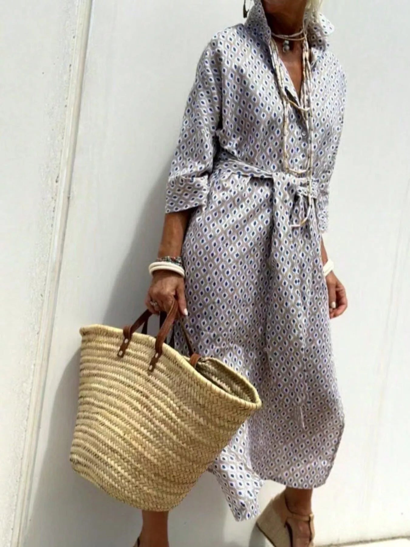 Person wearing a patterned outfit holding a woven bag against a white background