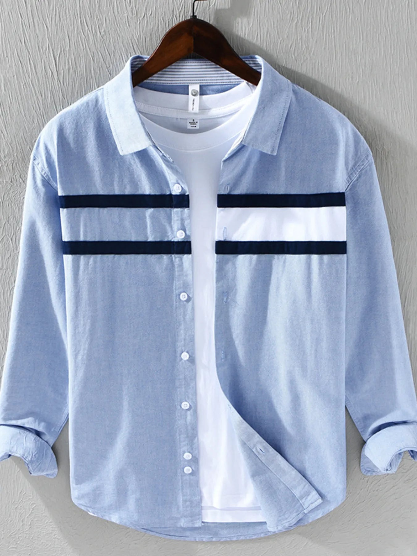 Light blue button-up shirt with white collar and black stripes on a hanger against a gray background