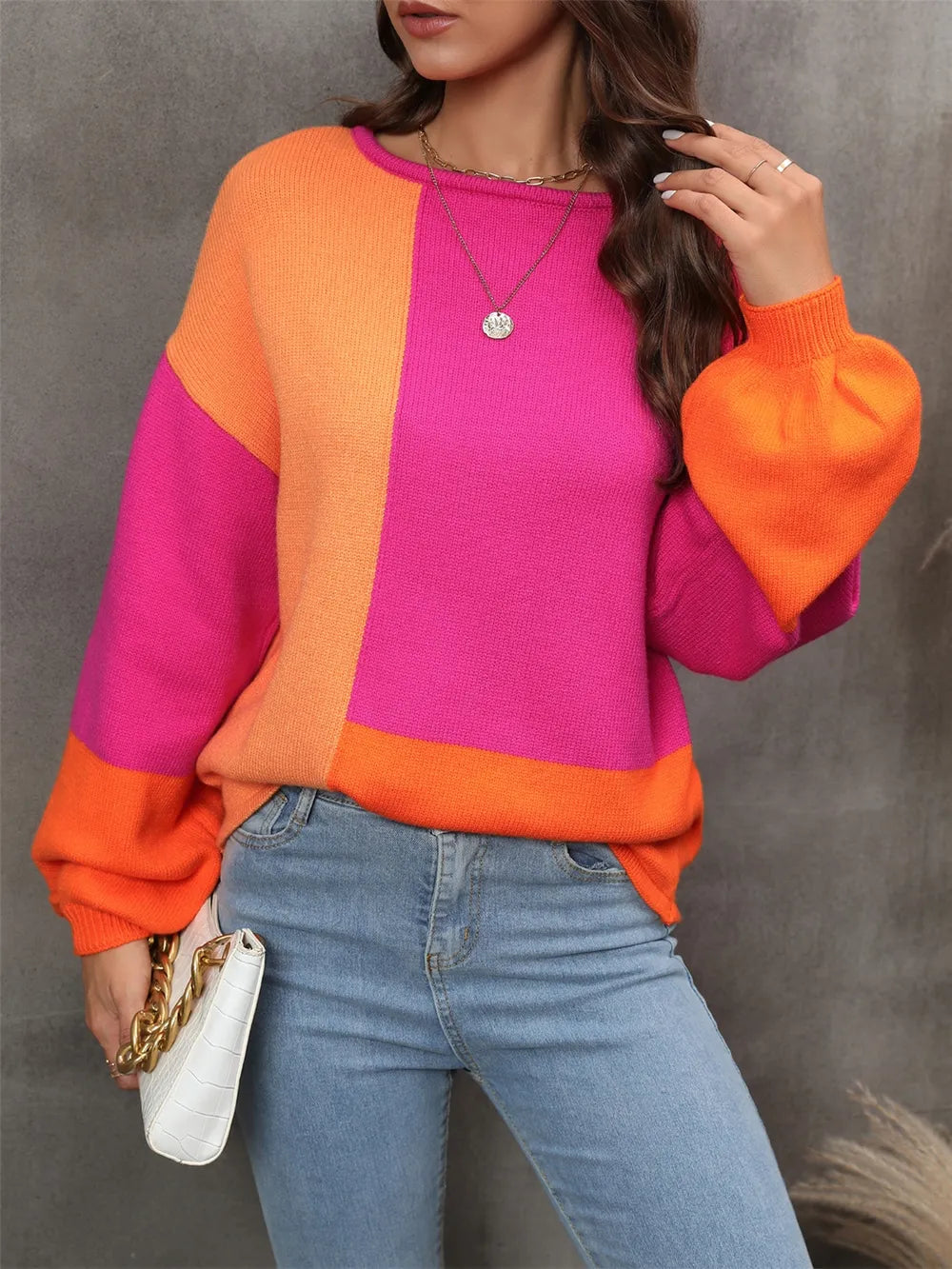Person wearing a colorful sweater with pink and orange sections, paired with blue jeans against a gray background.