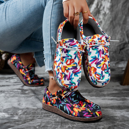 Colorful patterned shoes held by a person wearing jeans on a gray surface.
