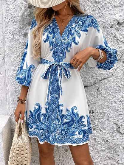 Woman wearing a white dress with blue floral patterns against a textured wall.