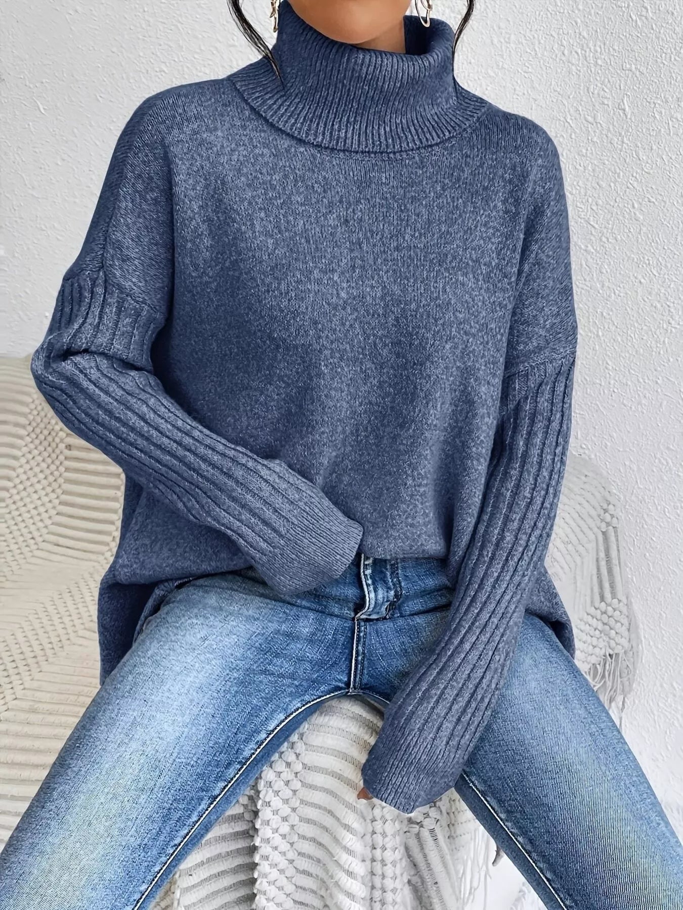 Person wearing a blue turtleneck sweater and jeans sitting on a textured surface.