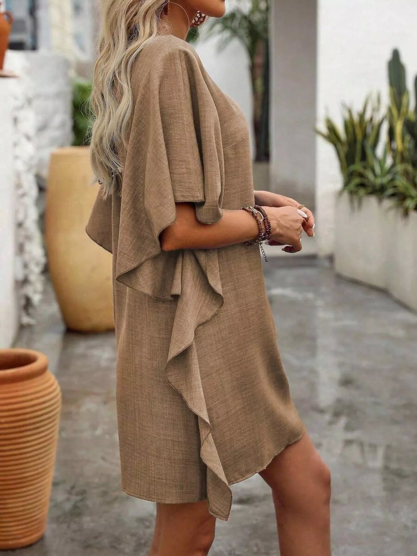 Woman wearing a beige dress standing outdoors with plants in the background